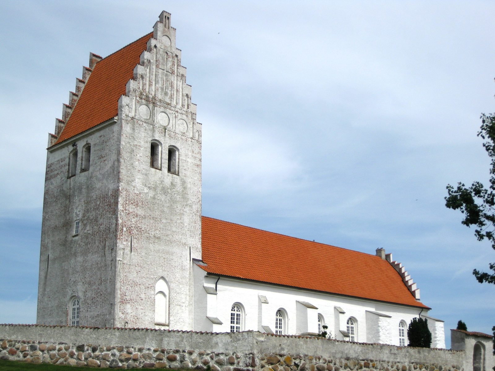 Fanefjord Church with a stepped brick gable and red roof behind a fieldstone wall