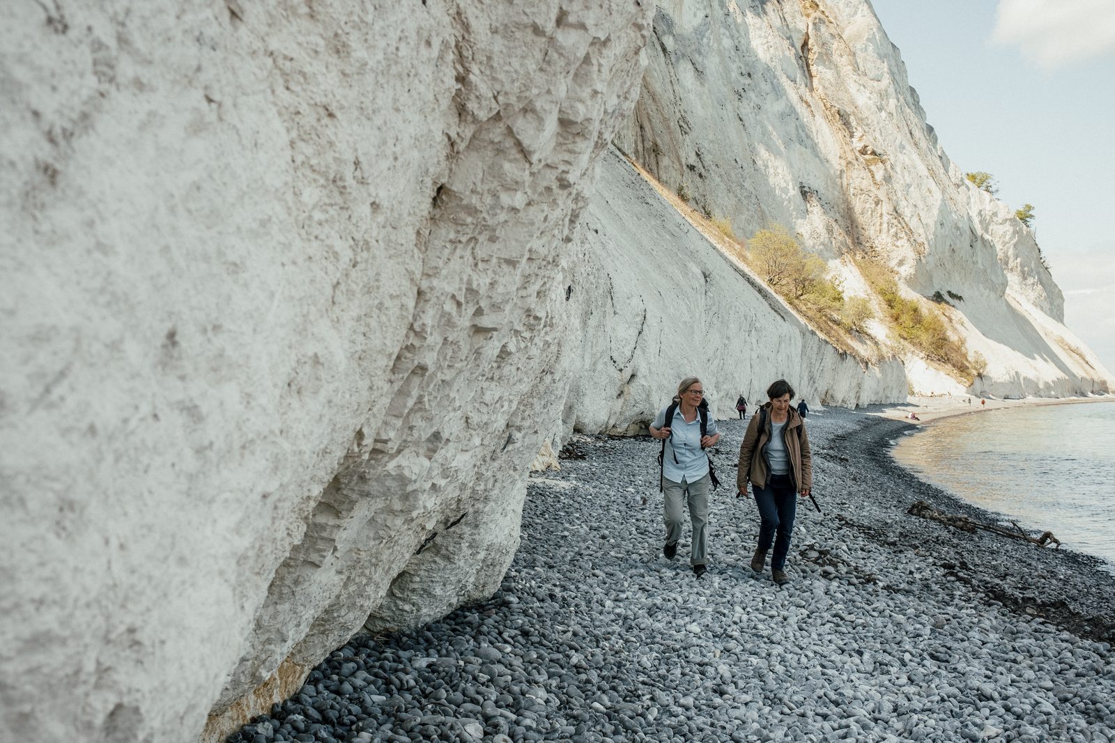 Two hikers walking on the pebble beach below the chalk cliffs of Møns Klint