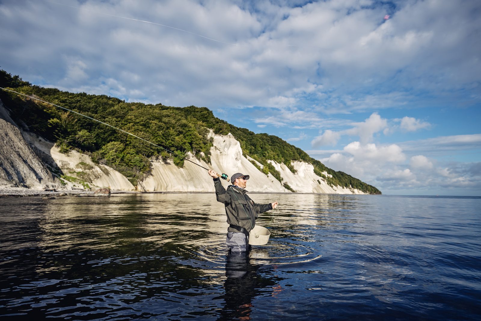 Angler wading in the Baltic Sea and casting a fly rod in front of the chalk coast of Møns Klint