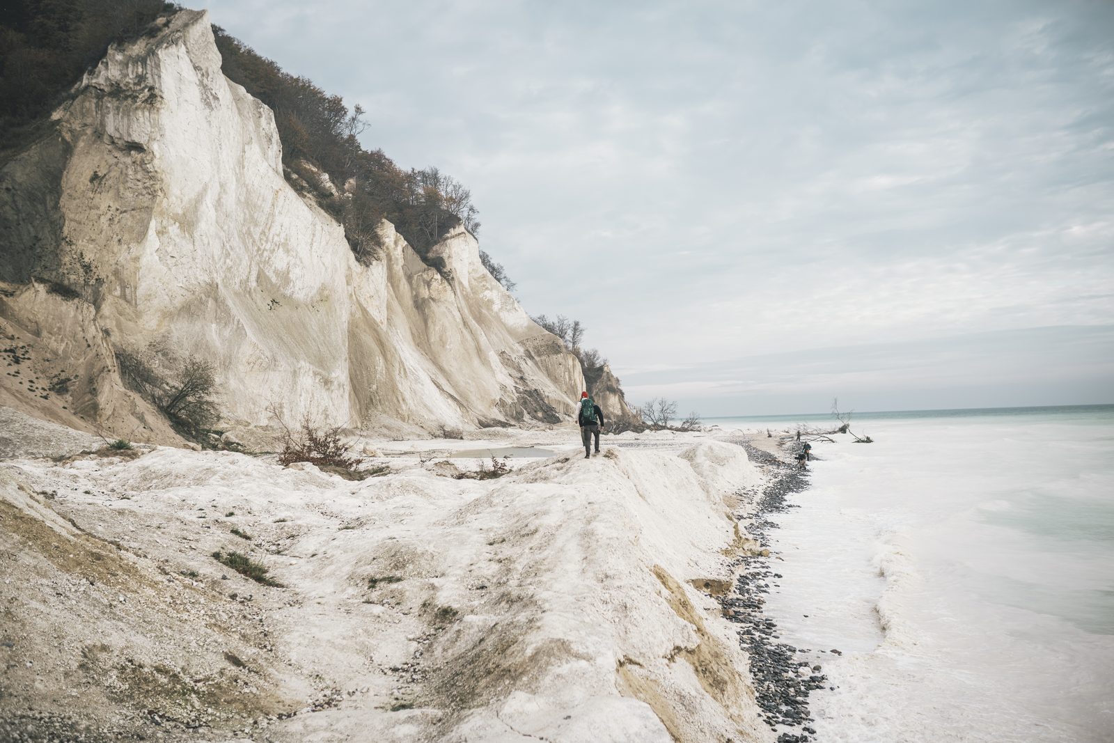 Person with a backpack walking along the beach below the chalk cliffs of Møns Klint