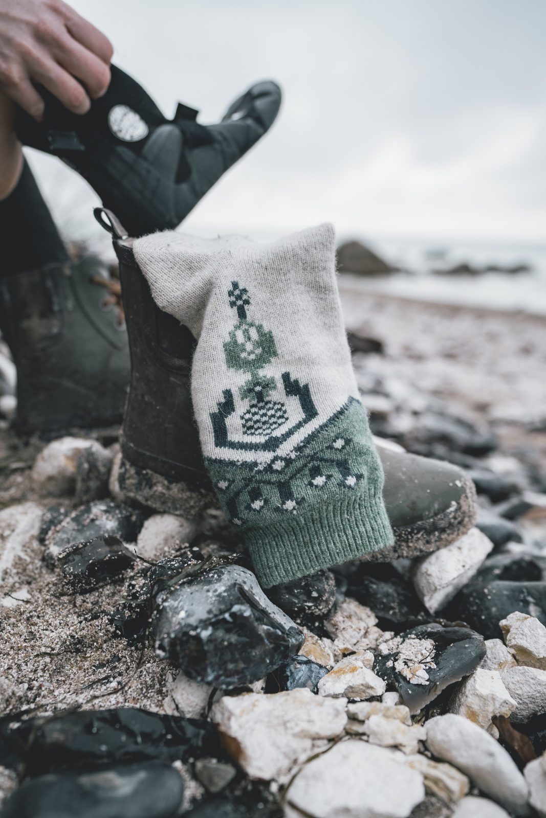 Rubber boot with a knitted sock and a neoprene glove on flint and chalk stones on the beach