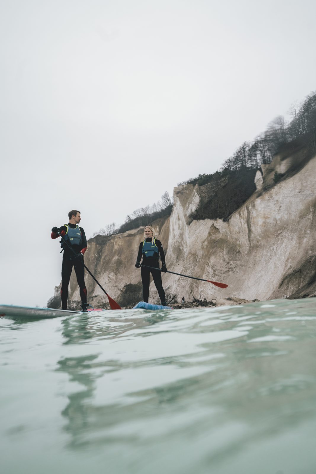 Two people in wetsuits on stand-up paddleboards in front of the chalk cliff of Møns Klint