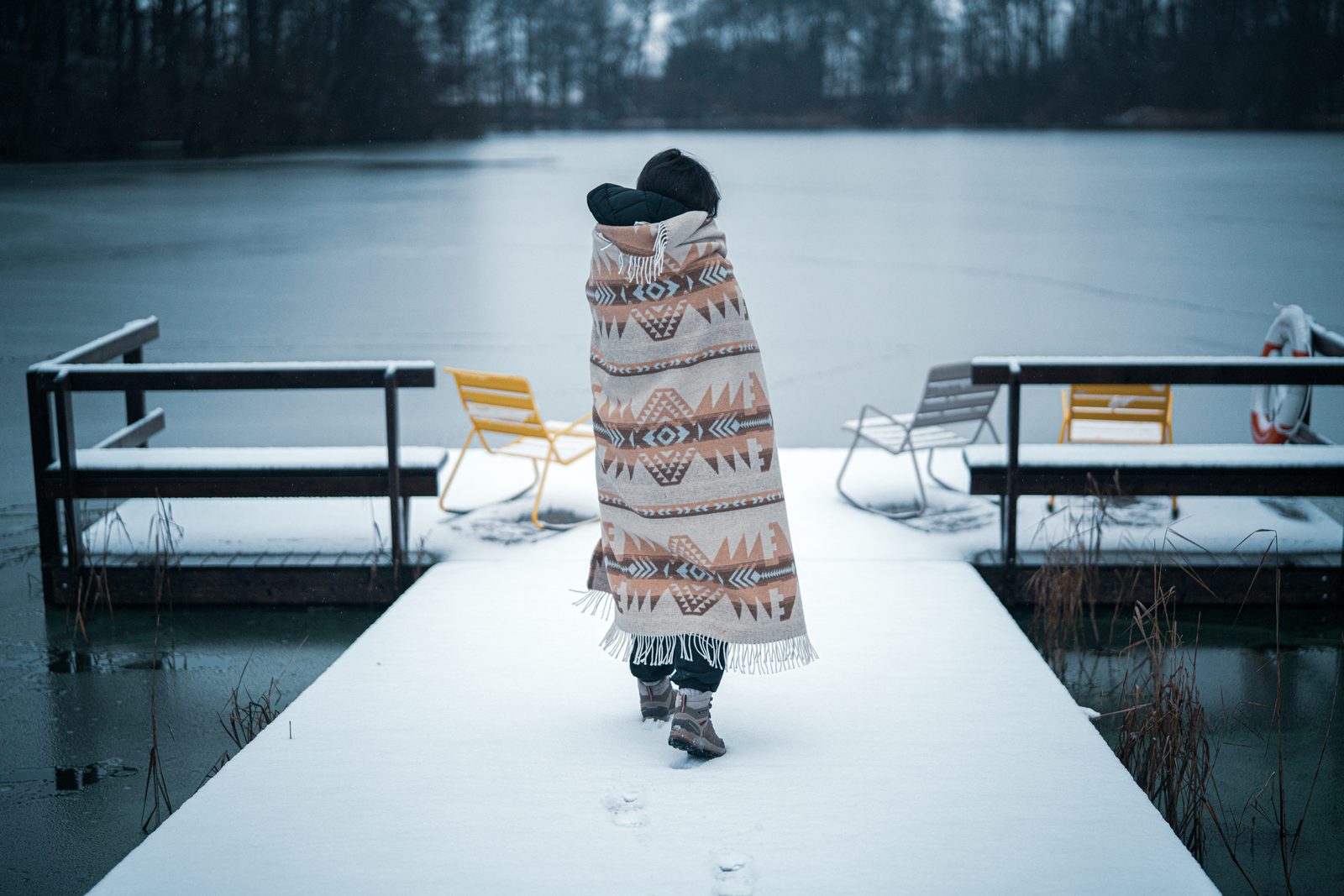 Person wrapped in a blanket walking along a snowy jetty by a frozen lake on eastern Møn