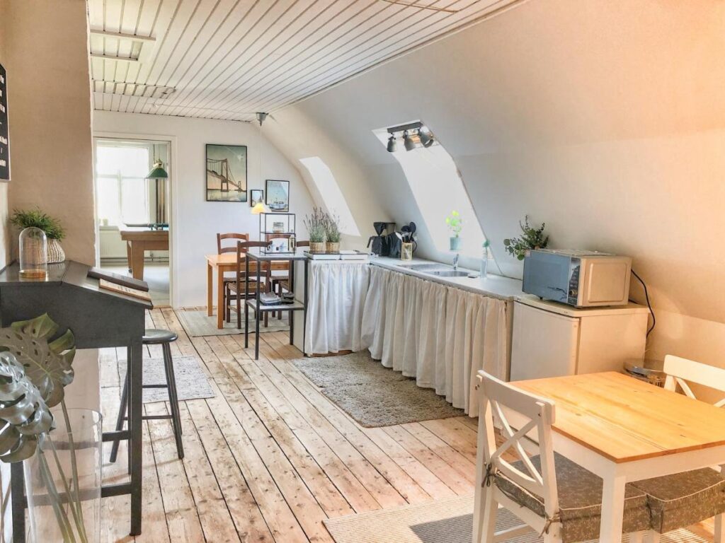 Helles, luftiges Küchen- und Esszimmer im Dachgeschoss des Maglebjerggaard Bed & Breakfast. Der Raum ist mit einem Holzfußboden ausgestattet und verfügt über eine Essgruppe sowie eine einfache Küchenzeile. Die schrägen Decken und großen Fenster sorgen für eine gemütliche, einladende Atmosphäre.